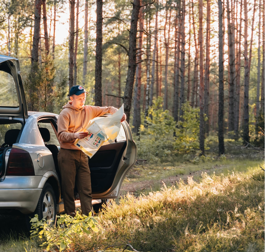 A man leaning on the car door is reading a paper.