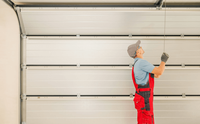 A person in red overalls and hat working on a garage door Description automatically generated with low confidence