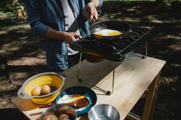 man holding frying pan cooking eggs outdoors